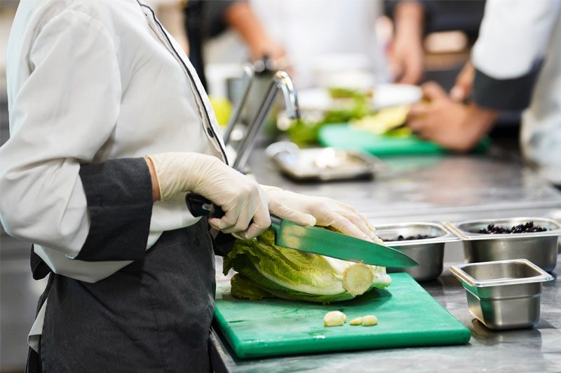 Mains de cuisinier coupant des légumes