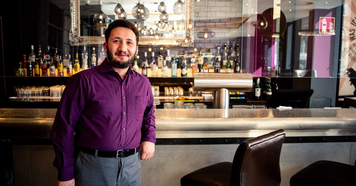 Professionally dressed barman standing in front of an elegant bar