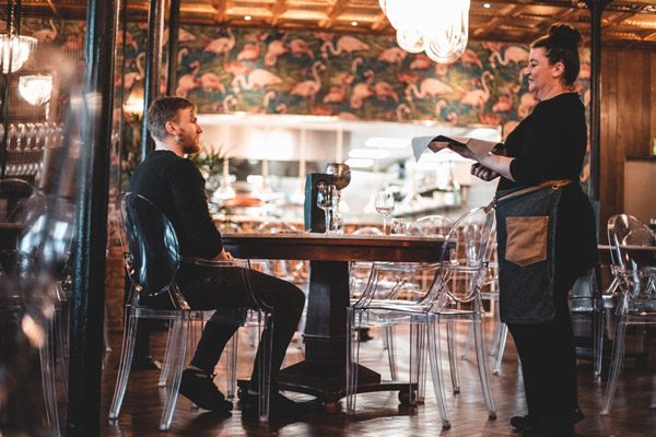 Waitress holding a serving plate while chatting with a customer seated at a table