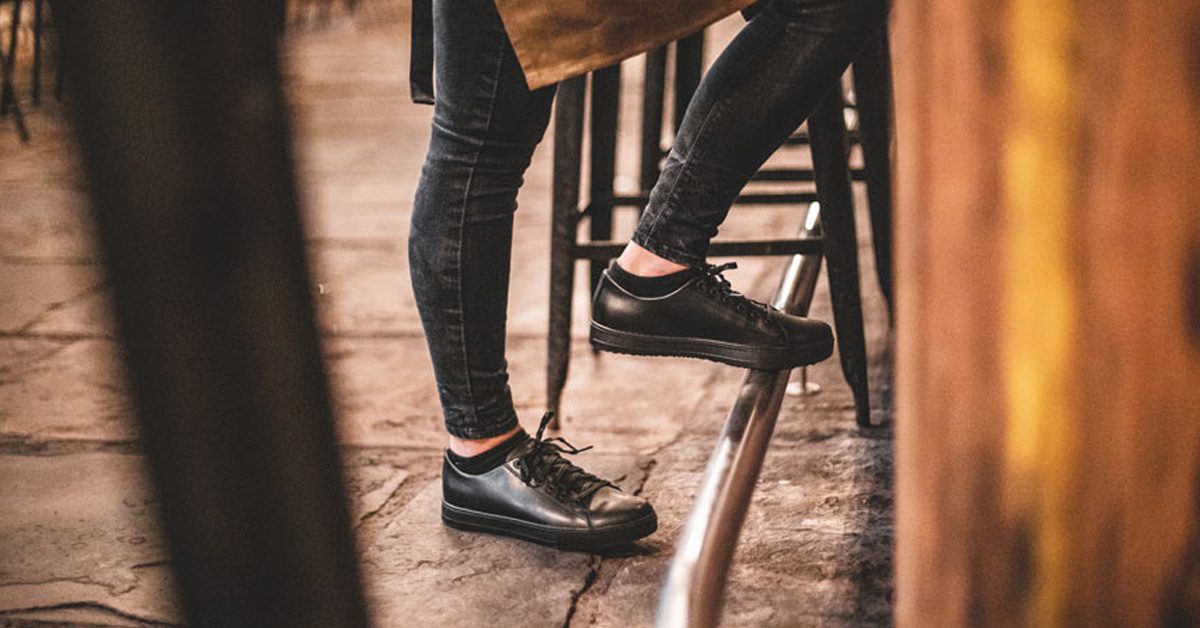 Woman wearing black slip-resistant restaurant shoes with foot balancing on metal bar