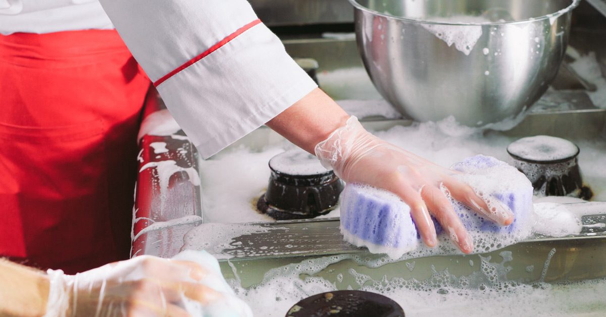 Two chefs cleaning the industrial-sized stove inside a restaurant with chemicals