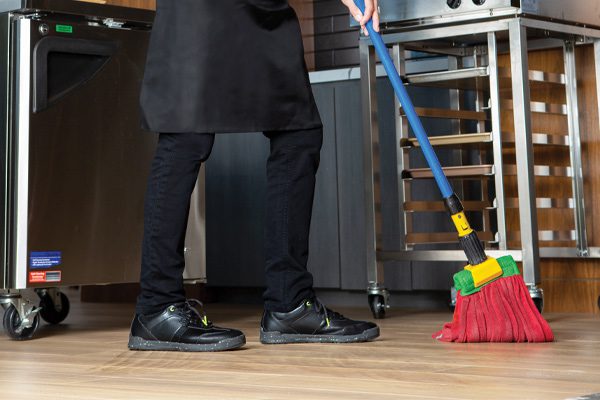 Waiter mopping parquet floor in front of kitchen equipment while wearing black slip-resistant work shoes