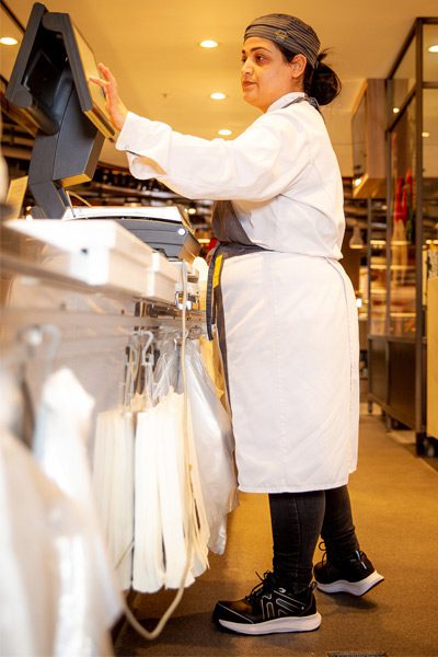 Butcher wearing black, slip-resistant Colly shoe style behind register at supermarket