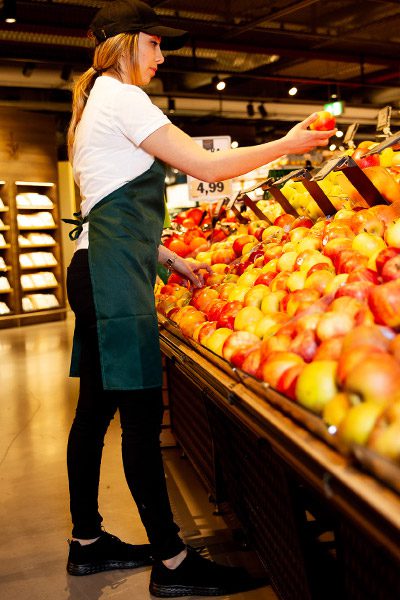 Store assistant stocking apples onto stand wearing lightweight Everlight style