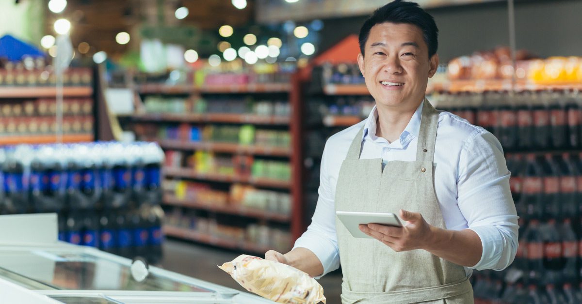 Smiling supermarket manager holding a notepad and a bag of frozen food while checking inventory at his store