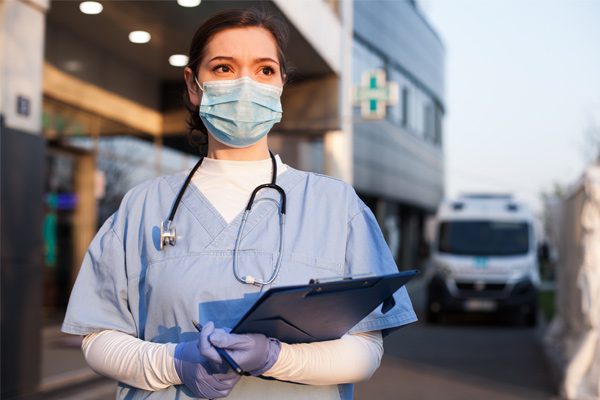 Young doctor standing in front of ICU hospital wearing full PPE and holding clipboard