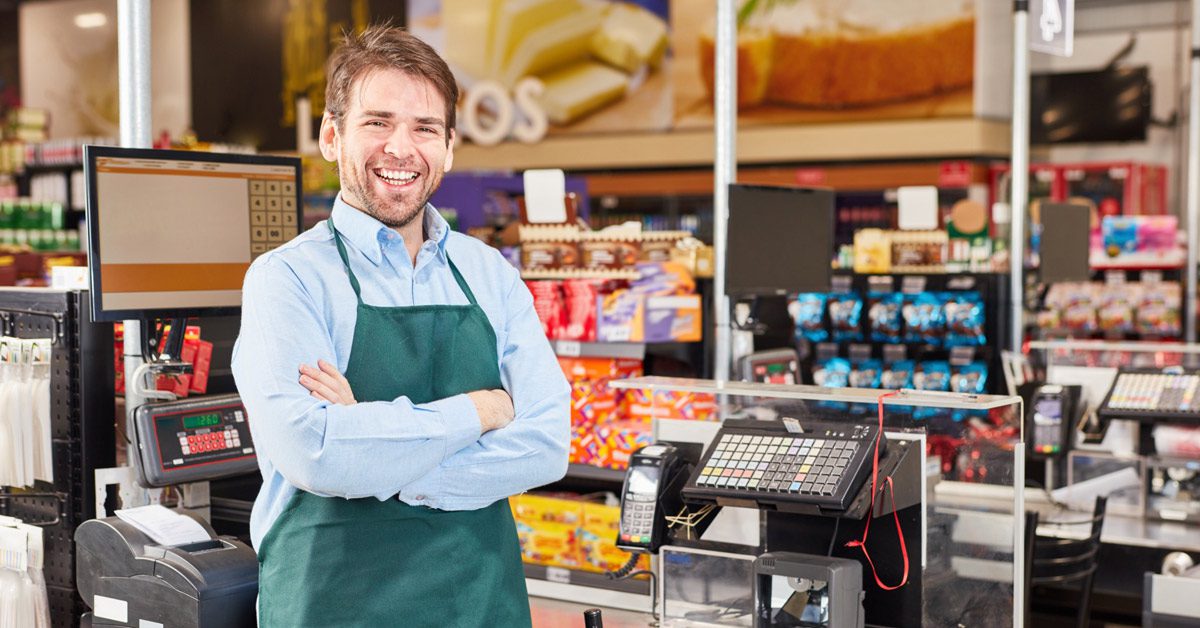 Smiling cashier standing with arms crossed behind till in retail shop
