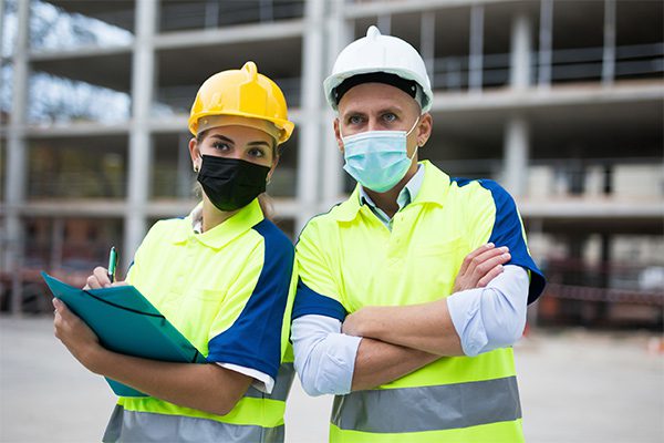 Male and female engineers wearing reflective safety gear, hard hats and masks at work site