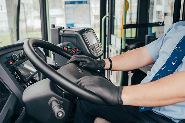 Bus driver wearing black leather gloves with hands on steering wheel