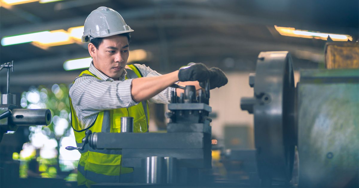 Manufacturing worker operating machinery wearing white and yellow safety gear