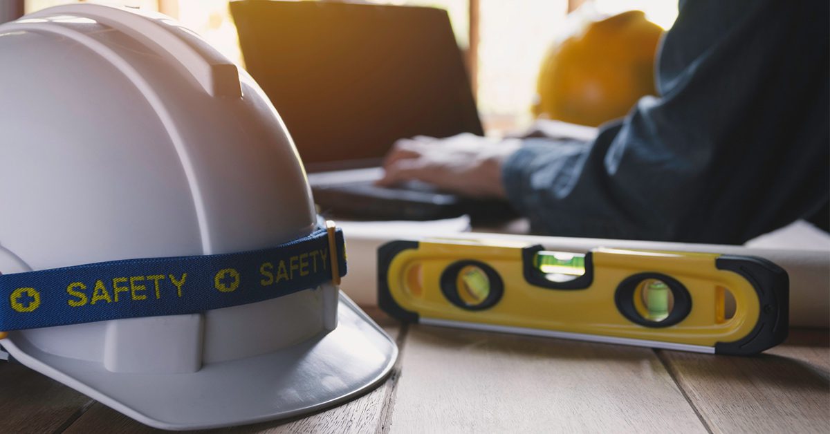 Man working at laptop on table next to yellow and white hard hats and a level