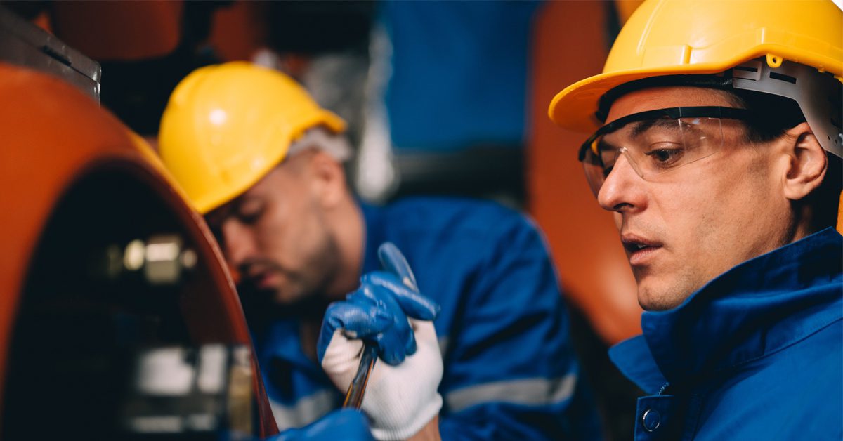 Two workers wearing hard hats and safety gear while operating and testing machinery