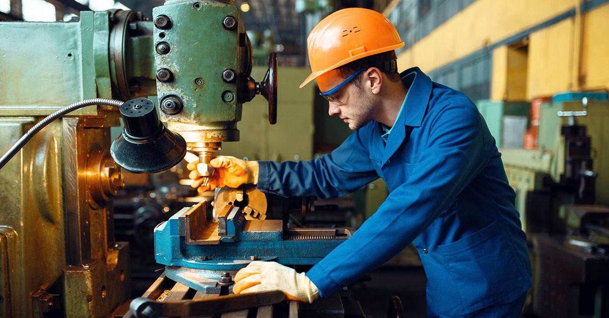 Technician operating machinery inside a manufacturing plant wearing safety goggles, hard hat and protective gloves