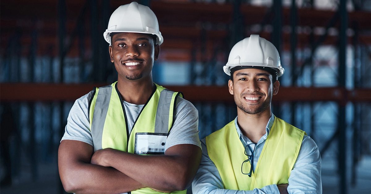 Two contractors inside a warehouse with arms crossed wearing protective gear