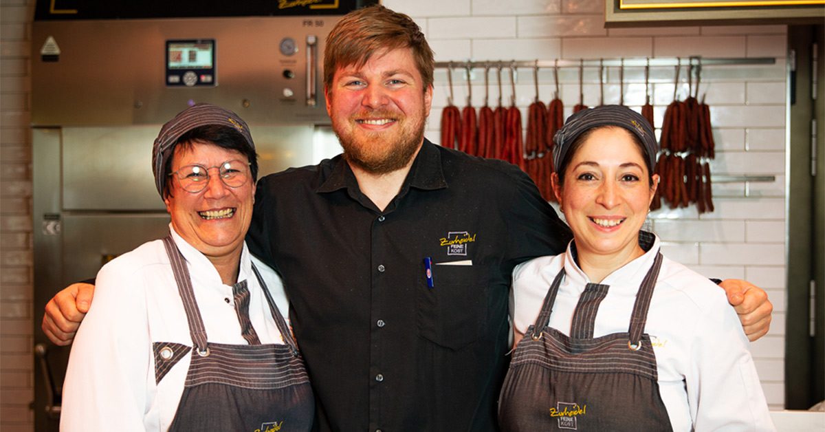 Group of three staff members smiling and standing behind butcher’s counter