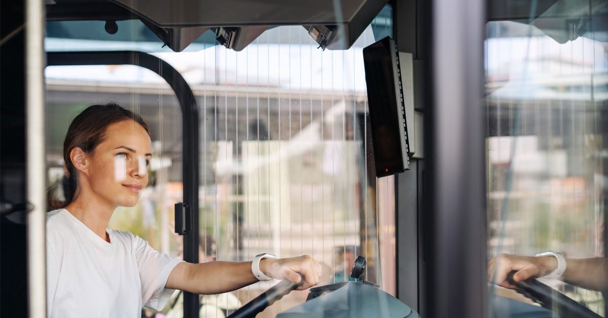 Conductora de autobús sonríe con las manos en el volante