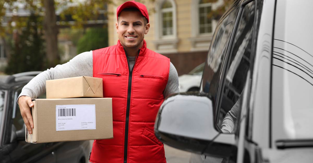 Courier with parcels in hand standing next to delivery van