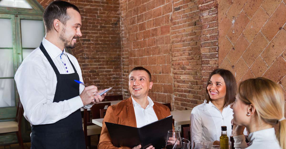 Un camarero sonriente toma nota a los clientes en un restaurante