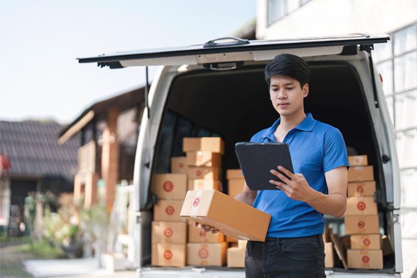 Delivery worker standing behind van full of boxes and holding a tablet