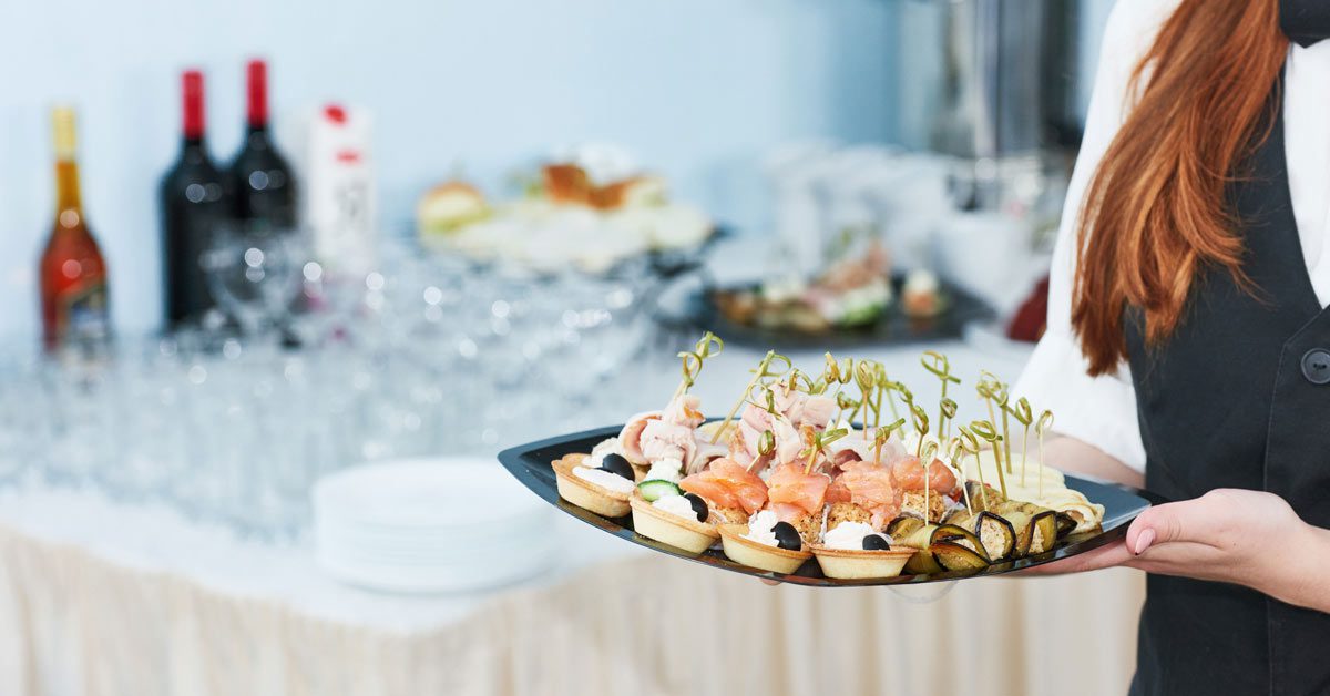 Una profesional del catering lleva una bandeja con canapés  