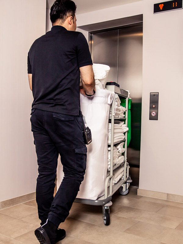 Saloon_Black_HouseKeeper-(7) Employé d’un hôtel entrant dans l’ascenseur avec un chariot de linge