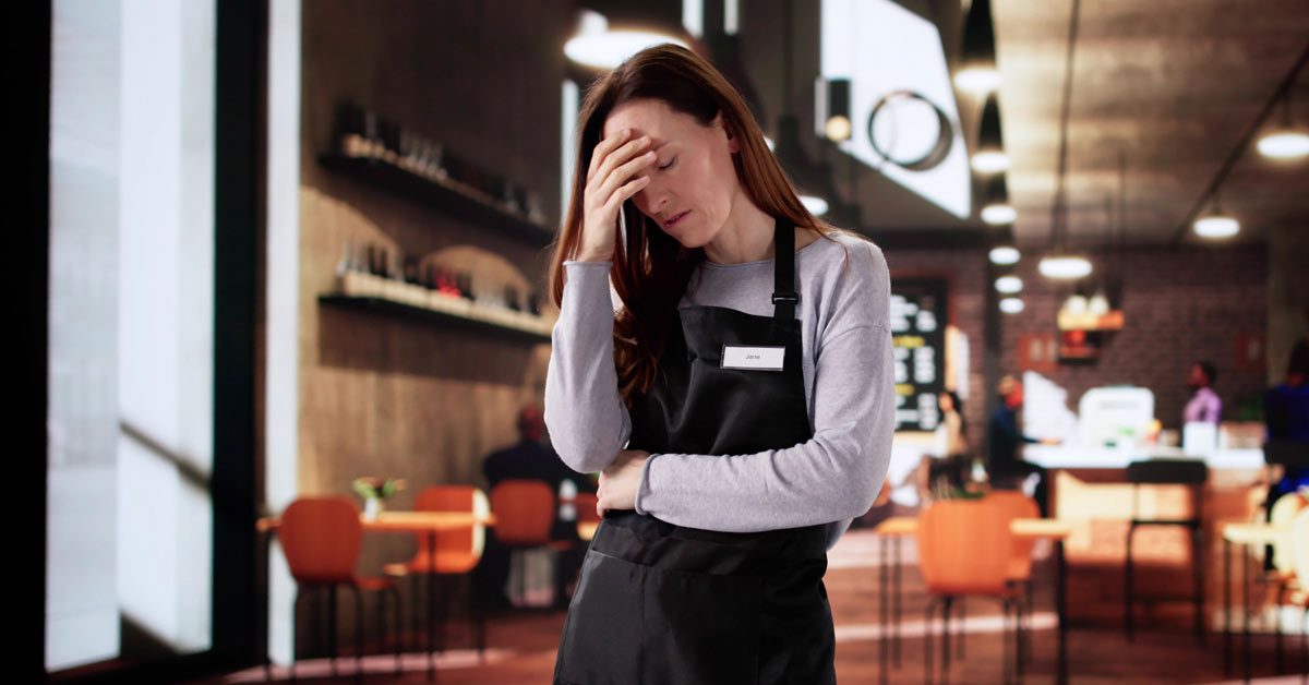 Employée du secteur de la restauration qui se tient la tête comme signe de maladie